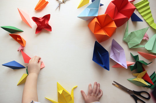 the child makes origami. Multicolored Origami and paper on  a white table. origami lesson
