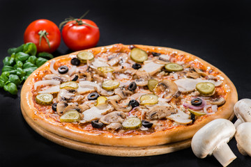 Appetizing fresh pizza with mushroom, bacon, olives, onion and pickled cucumbers on wooden board on dark background