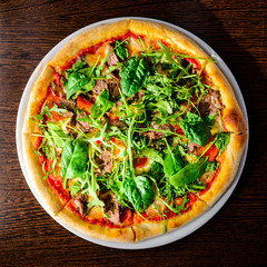 Appetizing Italian pizza with meat, tomatoes, cheese and basil leaves on the wooden table. Top view, flat lay
