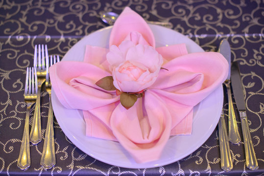 Formal table setting with silverware placed in the order of use, and elegantly wrapped napkin in the shape of a flower on top of white china, ready for guests at an event, wedding or at a restaurant