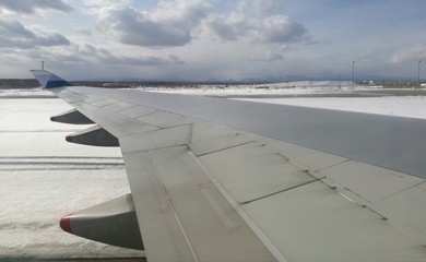 Airplane wing taken from plane window, moving on ground at an airport, mountain background, blue...