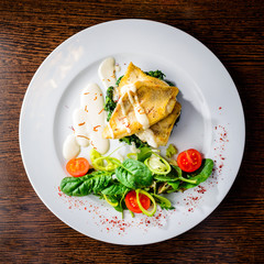 Delicious fish served with tomatoes, lemon and herbs on the wooden board. Top view, flat lay