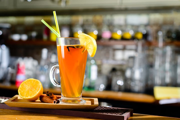Orange alcoholic cocktail in a glass with lemon and straws at bar counter