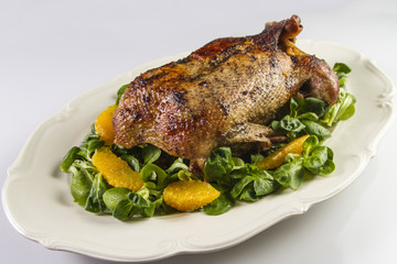 Baked duck in oranges and field salad or lamb's lettuce on white plate.