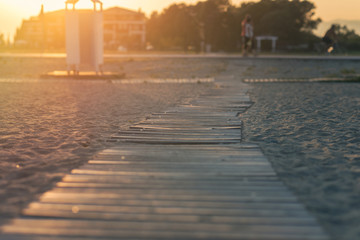 Wooden path on the beach in the rays of the setting sun.