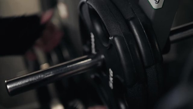 Closeup macro close up of handsome bodybuilder guy prepare to do exercises with barbell in a gym, keep barbell plate in hands, sport man