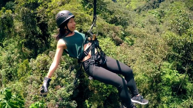 Experience the thrill of an Asian tourist sliding on a zipline over the lush forest in the breathtaking mountains of Baños,Ecuador.