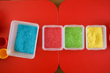 Sensory bin for toddlers with colourful rice on red table. Universal educational game