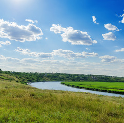 green meadow with river and cloudy sky in blue sky