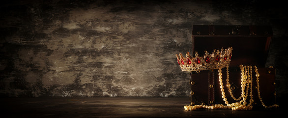 Image of mysterious opened old wooden treasure chest with light and queen/king crown with red...