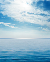 blue sea and clouds with sun over it in sky