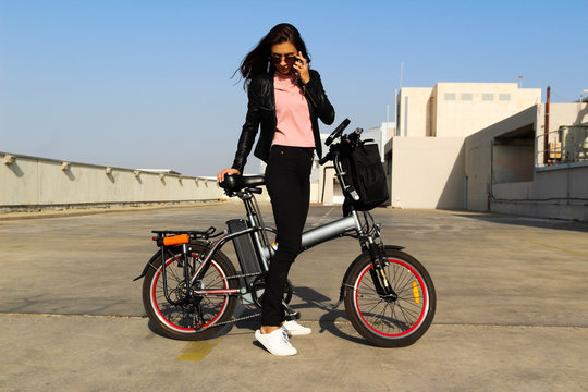 A young woman with an electric bicycle is talking on the phone