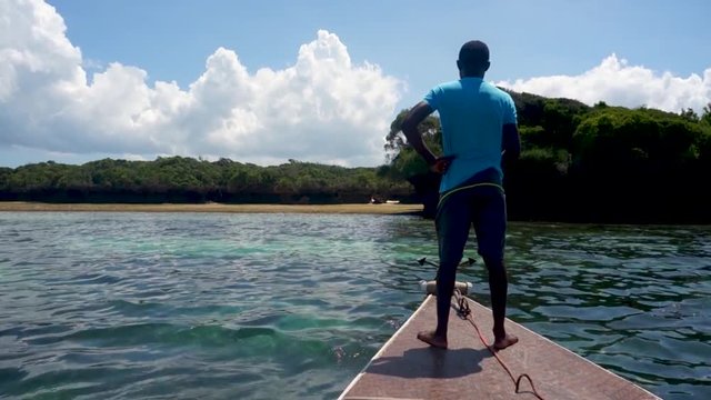 young barefooted African man on a wooden boat moored on the shore of a deserted tropical island