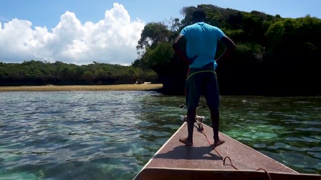 young barefooted African man on a wooden boat moored on the shore of a deserted tropical island