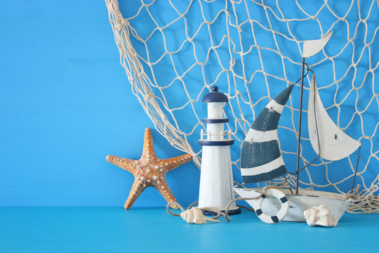 nautical concept with white decorative sail boat, lighthouse, starfish, seashells and fishnet over blue wooden table and background.