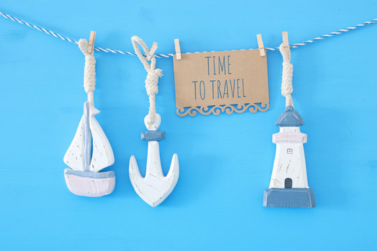 nautical concept with sea lifestyle decorations: sail boat and anchor hanging on a string over blue wooden background.