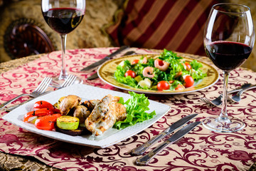 Romantic dinner at a restaurant. Two appetizing dishes with shrimp and baked vegetables and glasses with wine