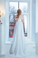 Невеста стоит у окна в белом платье
