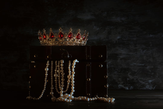 Image of mysterious opened old wooden treasure chest with light and queen/king crown with red Rubies stones. fantasy medieval period. Selective focus
