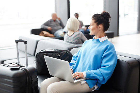 Young businesswoman in blue pullover sitting in airport lounge and working in the net while waiting for flight
