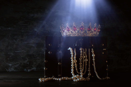 Image of mysterious opened old wooden treasure chest with light and queen/king crown with red Rubies stones. fantasy medieval period. Selective focus