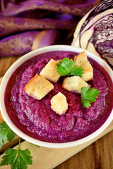 Cream soup made of red cabbage with croutons and parsley on wooden table