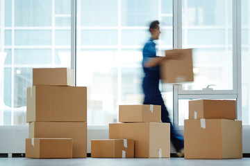 Blurred motion of contemporary worker with packed box walking to new office while delivering it to...