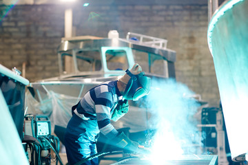 Engineer or welder in workwear carrying out his work in production department of shipbuilding...