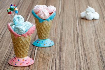 blue and pink meringue in the pink and blue cones with cupcakes on wood background and white meringues