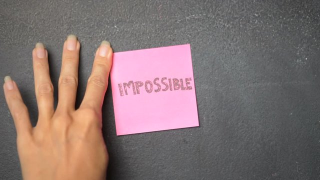 Closeup woman's hand sticking note with Impossible word on the blackboard - video in slow motion