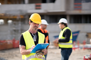 Foreman at work on construction site checking his notes and drawing plan on clipboard