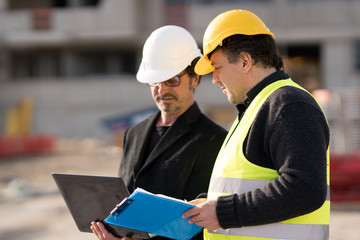 Civil engineer giving instructions to a construction worker using a computer laptop. Outdoors