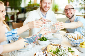 Company of friends toasting with glasses of fresh homemade lemonade over served table during festive dinner
