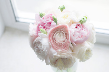 Gorgeous bridal bouquet of pink peonies Sarah Bernhardt, ranunculuses Hanoi, garden roses and white Eustoma in a vase on the window background. Wedding bouquet looks like a cloud