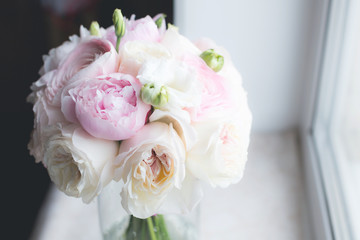 Beautiful bridal bouquet of pink peonies Sarah Bernhardt, ranunculuses Hanoi, garden roses and white Eustoma in a vase on the window background. Wedding bouquet looks like a cloud