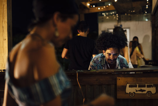Indian ethnicity with afro hair DJ controlling equipment and people dancing in a tropical party in the caribbean in Santa Marta, Colombia