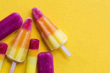 A selection of bright summer ice lollies on a yellow background