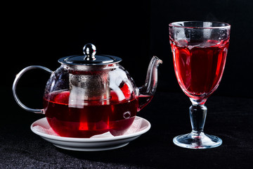 Glass teapot with hot red tea and high glass on dark background