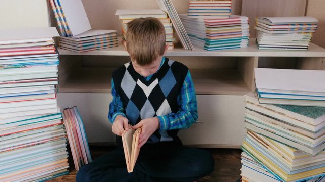 Boy reads a book sitting on the floor among the books.