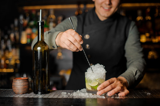 Barman stiring a fresh delicious cocktail with lime