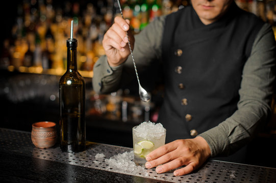Barman stiring a fresh delicious cocktail with lime and cane sugar