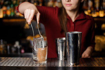 Bartender girl putting an ice cube into the decorated glass