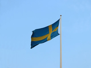 Two Color of Swedish Flag, yellow cross on blue color on blue sky background. Blown away by wind.