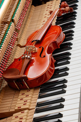 classic brown violin on the close up image of grand piano keys and interior showing strings, hammer...
