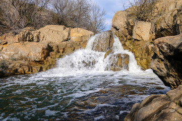 Boiling spring flow. Waterfall against the background of scanty vegetation.