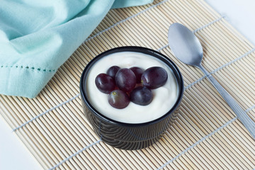 Yoghurt cup with black grapes and spoon close up