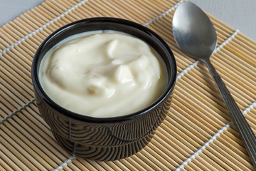Creamy fruit yogurt in black bowl on reed table mat close up