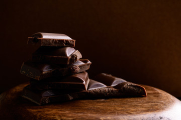 Bar of dark chocolate. Broken pieces of chocolate on wooden board over dark background