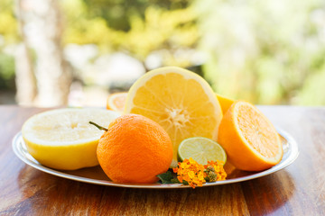 A metal dish with sliced ​​citrus on the background of the summer greenery of the garden on a vintage wooden table