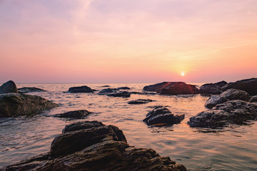 Obraz premium Tropical colourful sunset on the beach of Koh Chang island, Gulf of Siam, Thailand. View of dark night sea with protruding stones.